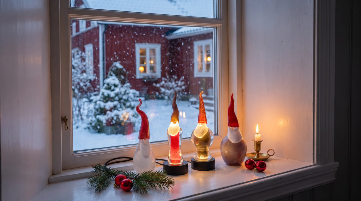 Handblåsta glastomtar i fönstret med snöfall och rött hus utanför